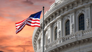 A view of the US capitol during sunset with a flag in the foreground.